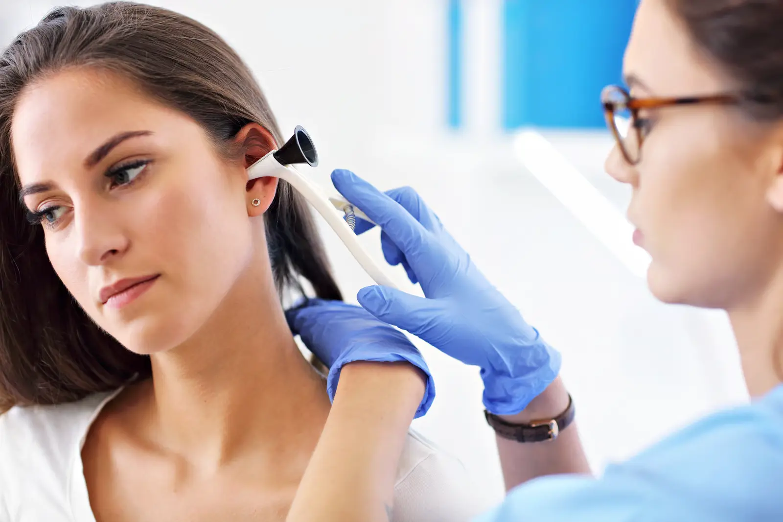 Pharmacist in blue gloves examining a woman’s ear with an otoscope to check for ear infection symptoms during a pharmacy consultation